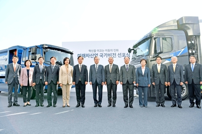 (앞 줄 왼쪽 네 번 째 부터) 이재명 경기도지사, 박영선 중소벤처기업부 장관, 성윤모 산업통상자원부 장관, 문재인 대통령, 정의선 현대차그룹 수석부회장, 홍남기 경제부총리 겸 기획재정부 장관, 김현미 국토교통부 장관 등이 수출형 수소전기트럭 및 수소전기청소트럭을 배경으로 기념촬영을 하고 있는 모습