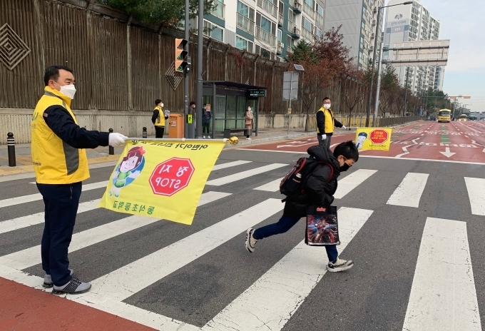 지난 26일 평택 동삭초등학교 앞에서 쌍용자동차 사내 사회공헌 프로그램 ‘네바퀴 동행’ 로고가 새겨진 안전조끼를 입은 쌍용자동차 임직원들이 등굣길 학생들의 보행 지도를 하고 있다.
