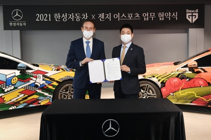 신사동에 위치한 한성자동차 AMG 브랜드 센터에서 진행된 한성자동차와 젠지 이스포츠의 업무 협약식에서 한성자동차 울프 아우스프룽 대표(왼쪽)와 젠지 이스포츠 이지훈 단장(오른쪽)이 협약서를 들고 기념 촬영을 하고 있다.
