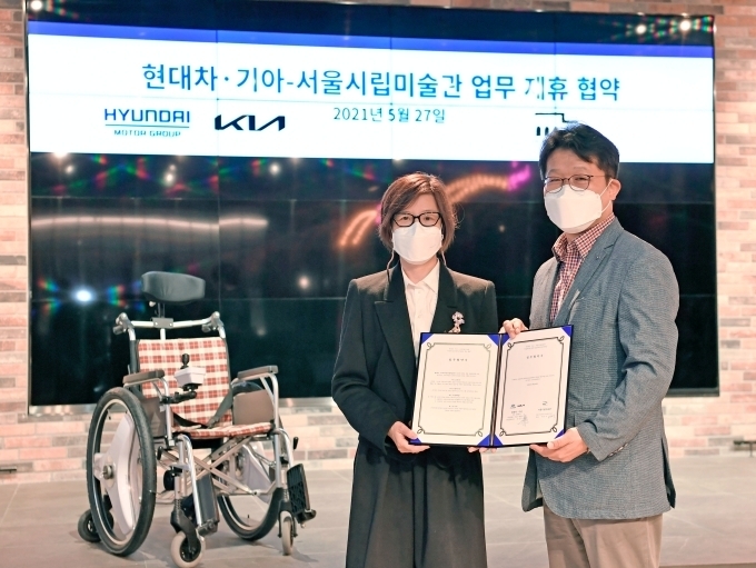 27일 서울 서초구 소재 제로원에서 진행된 업무협약(MOU) 체결식에서 (왼쪽부터) 서울시립미술관 백지숙 관장, 기아 신동수 경영전략실장이 자율주행 시스템이 탑재될 전동 휠체어 앞에서 기념 사진을 촬영하고 있다.