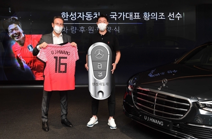 한성자동차 메르세데스-벤츠 청담 전시장에서 한성자동차 울프 아우스프룽 대표(왼쪽)와 대한민국 축구 국가대표 황의조 선수(오른쪽)가 지원받은 차량과 함께 기념 촬영을 하고 있다.