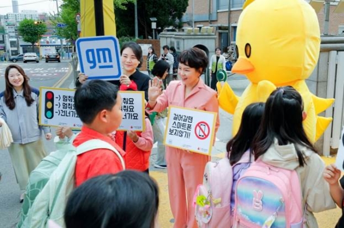 29일 인천 동수 초등학교에서 진행된 ‘안전하게 건너요’ 캠페인에서 GM 커뮤니케이션 총괄 및 CMO 윤명옥 전무(왼편)를 비롯해 GM 임직원 및 동수 초등학교 학생들이 등교하는 학생들을 대상으로 안전 구호를 외치고 있는 모습.